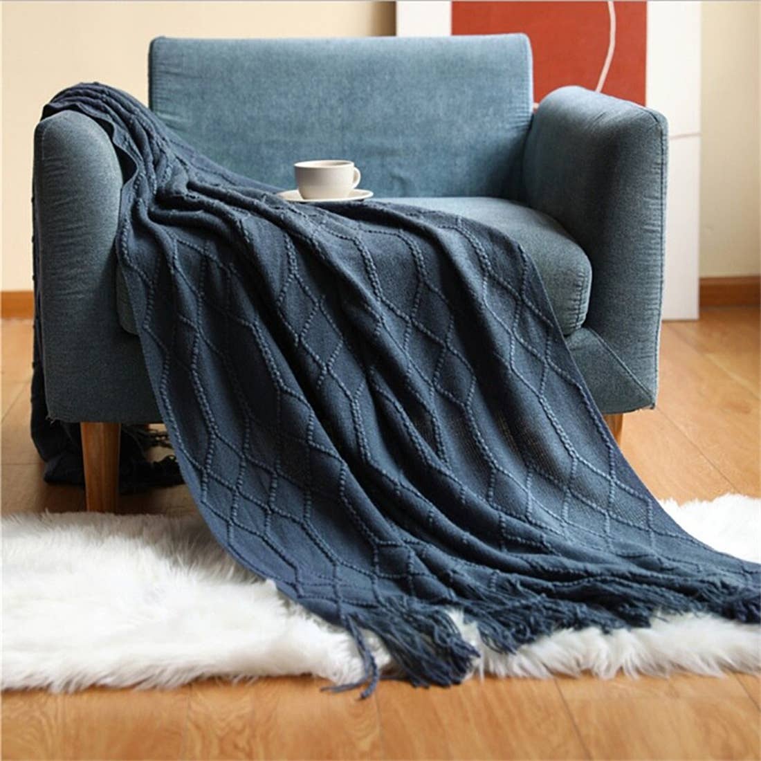 Blue textured throw blanket draped over a chair with a cup on a small table.