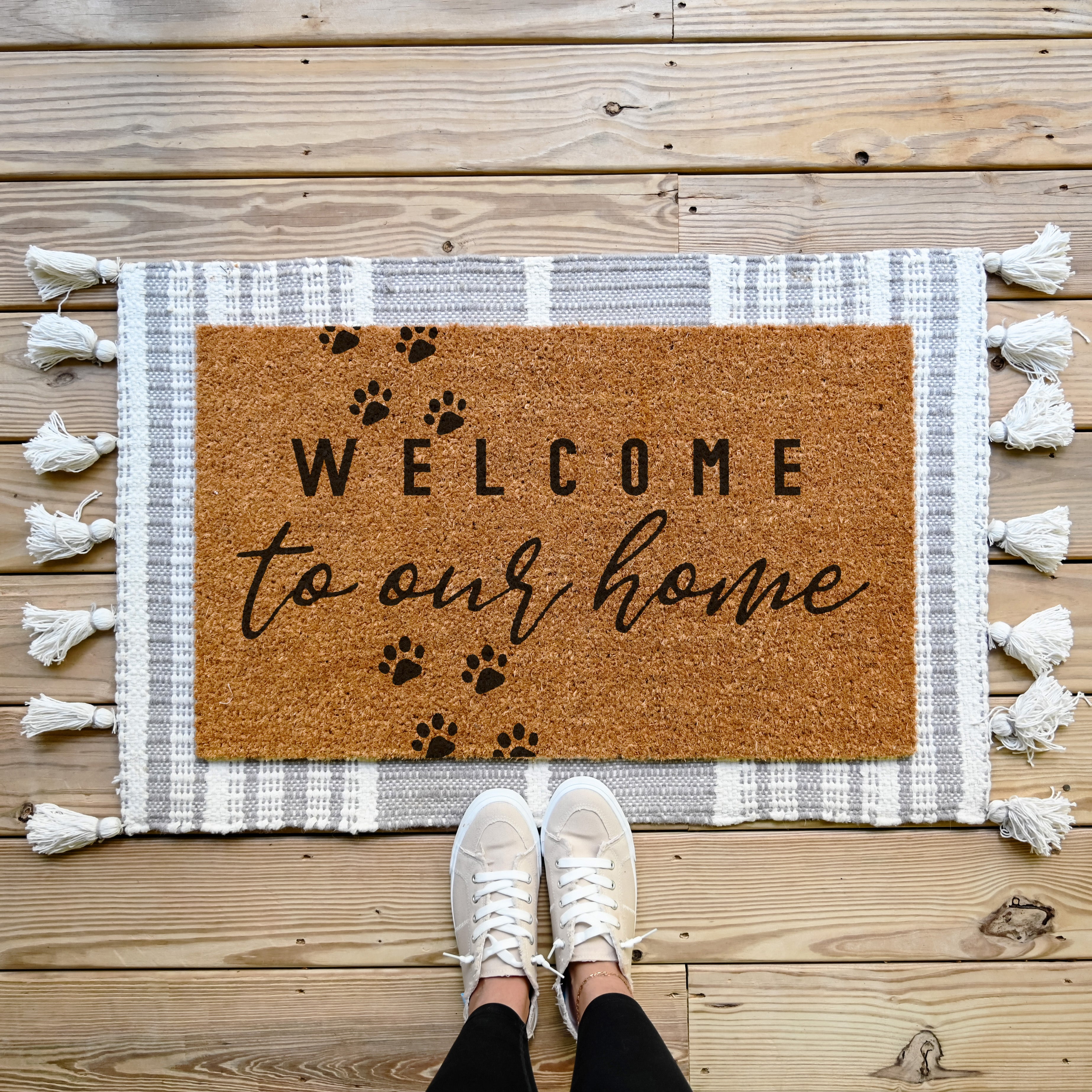 doormat that says welcome to our home in the middle. It has paw prints walking across the mat.  coir doormat.