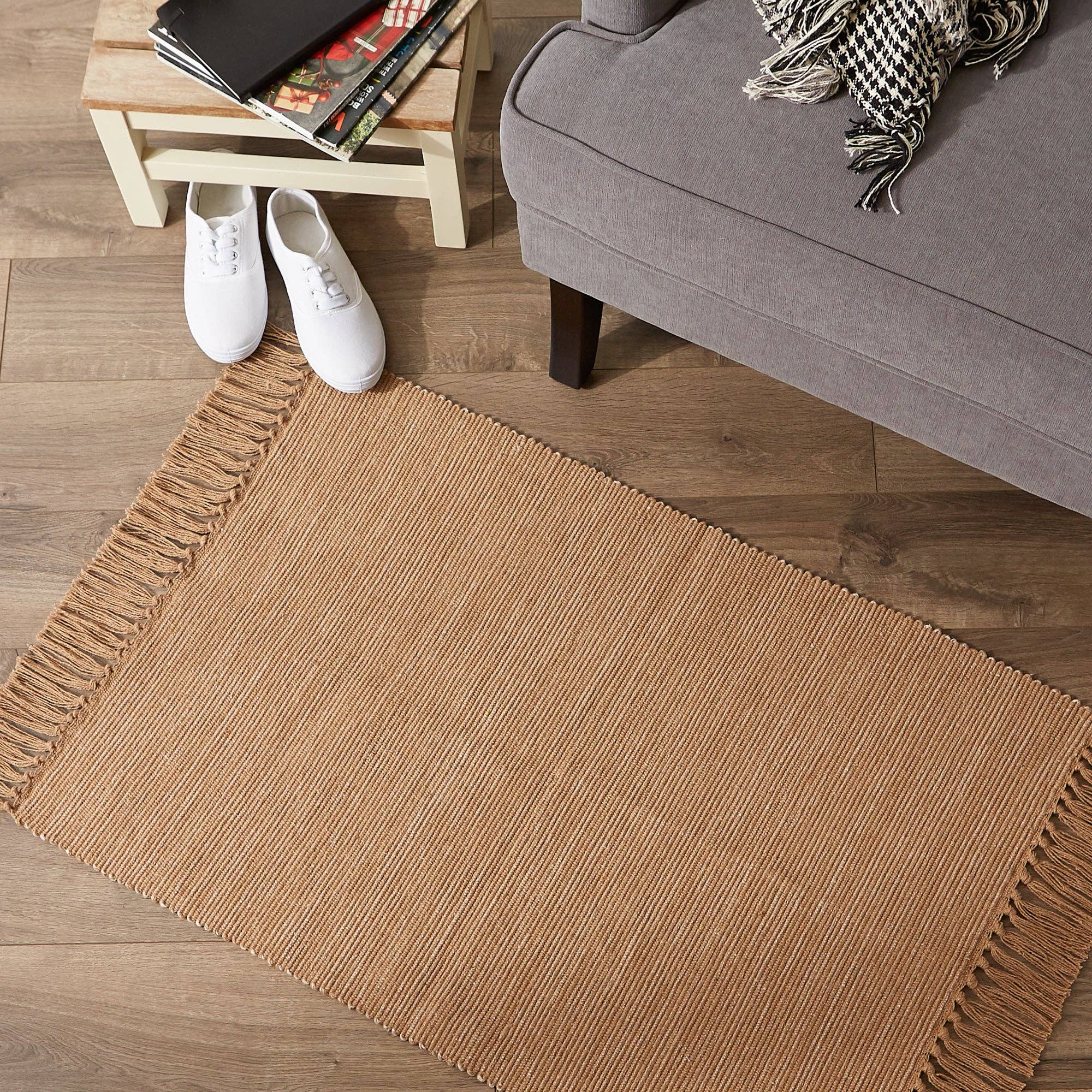 Brown woven rug on a wooden floor with a gray sofa and white shoes in the background.
