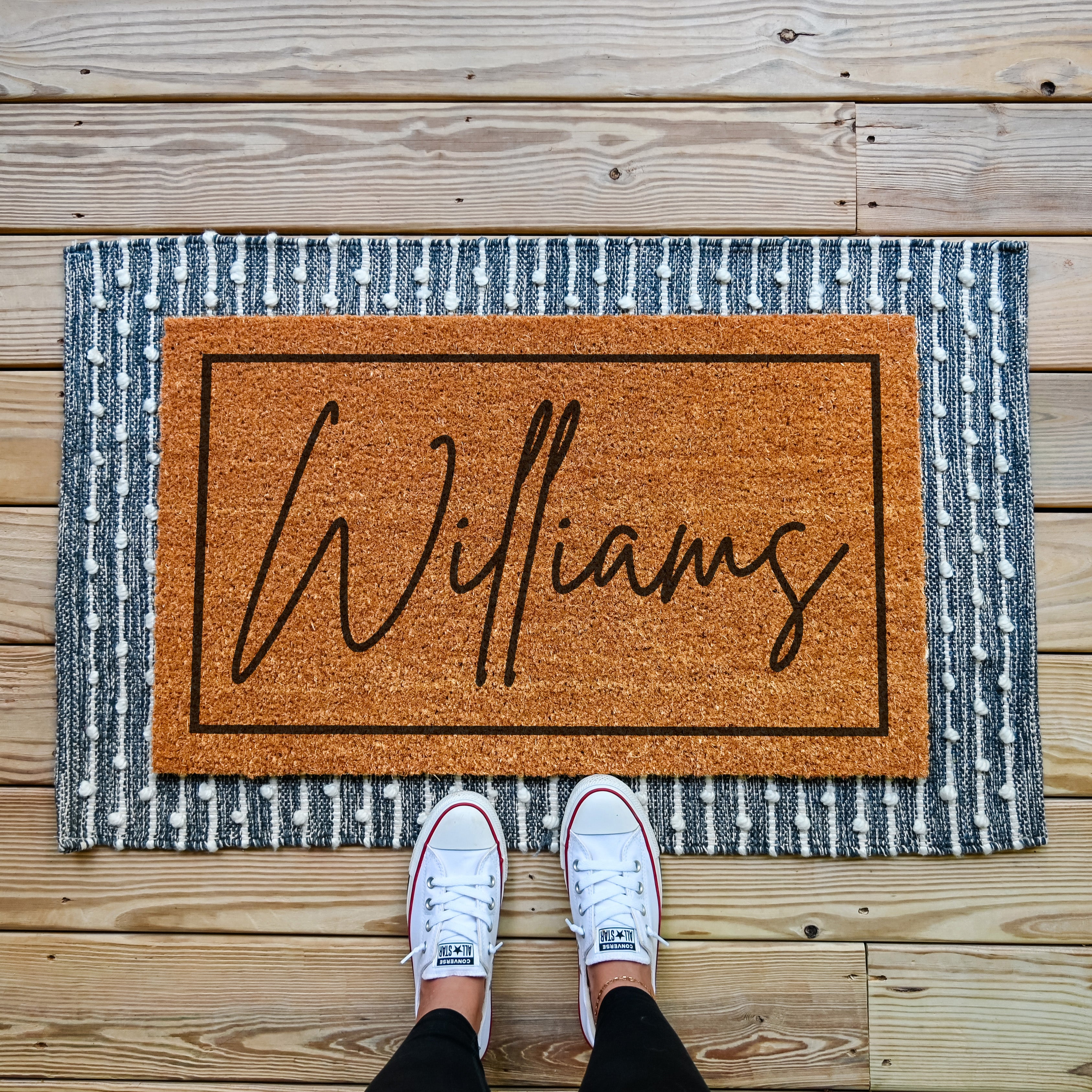 custom doormat with personalized last name in cursive. There is a thin border that runs around the edge.