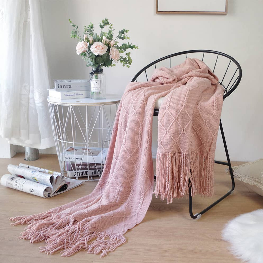 Pink knitted blanket draped over a black chair in a room with a white table and decor.