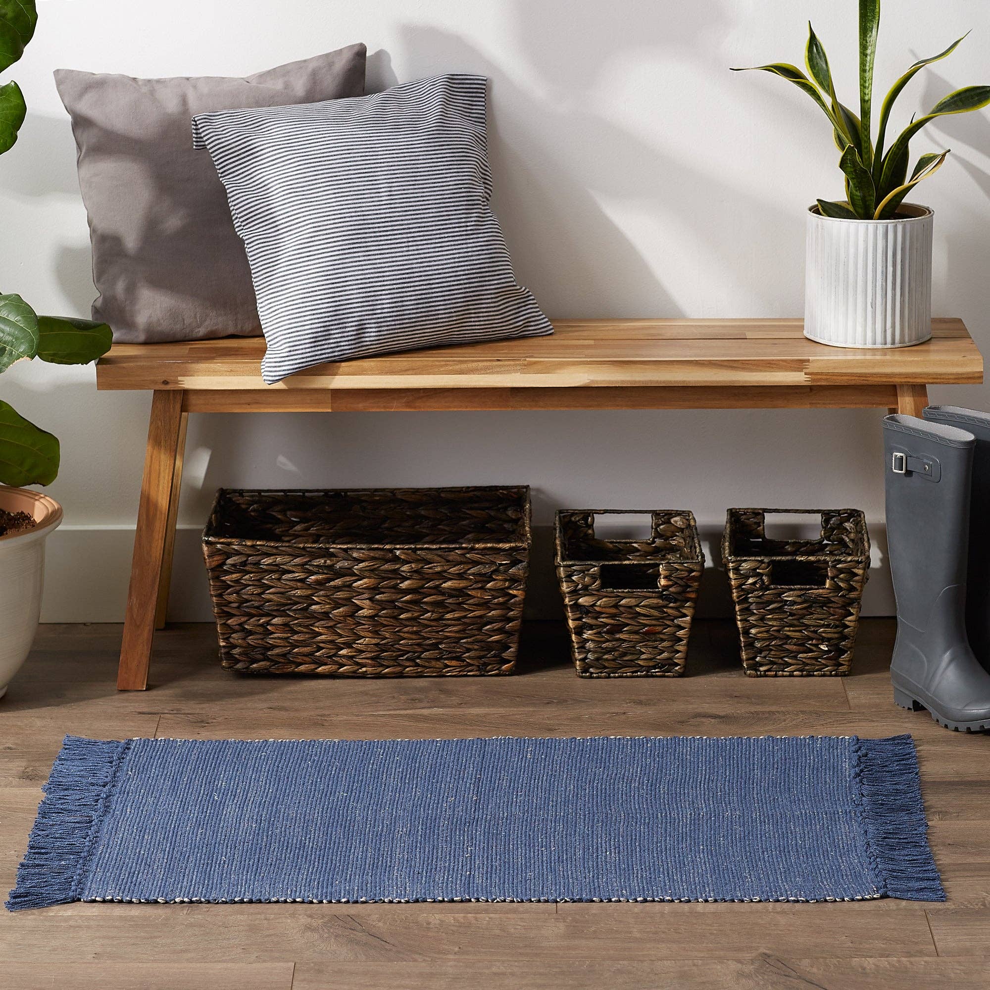 Wooden bench with pillows, wicker baskets, and a blue rug on a wooden floor.